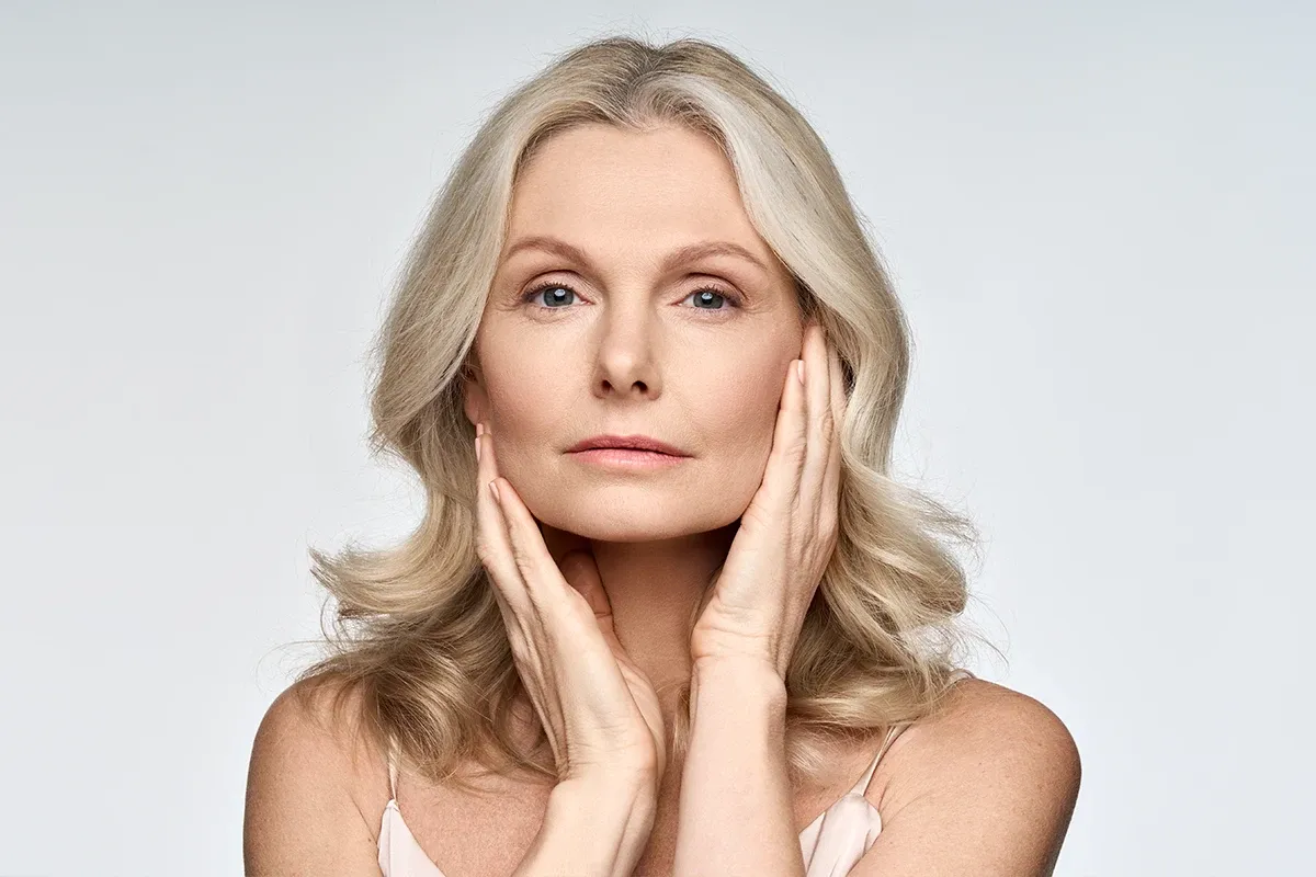 Mature woman framing her face with both hands, showing skin texture and aging changes during menopause